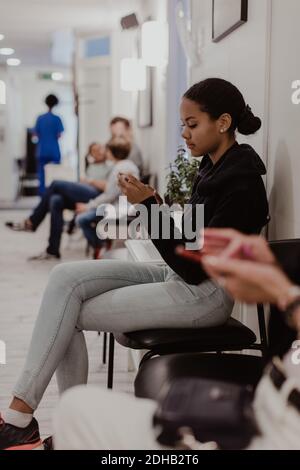 Fille utilisant un téléphone portable en attendant dans le couloir de l'hôpital Banque D'Images