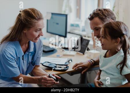 Fille souriante regardant un médecin montrant un glaucomètre en examen médical chambre Banque D'Images