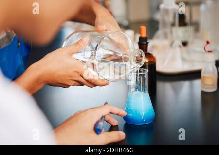 Image rognée d'étudiants multiethniques mélangeant des solutions au laboratoire de chimie à l'université Banque D'Images