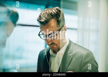 Homme professionnel attentif portant des lunettes et des écouteurs au bureau Banque D'Images