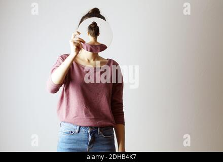 Qui suis-je ? femme tenant un miroir devant son visage. Sans visage, identité non reconnaissable, le miroir montre son dos. Cacher son visage Banque D'Images