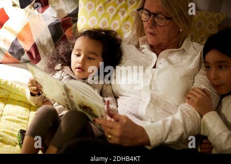 Vue en grand angle de la grand-mère lisant le livre aux petites-filles pendant couché sur le lit à la maison Banque D'Images