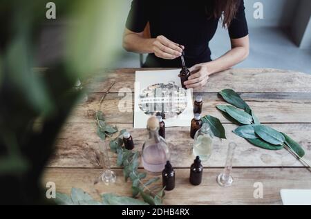 Section médiane du propriétaire femelle utilisant une pipette pour mélanger le liquide de bouteille tout en étant assis à la table dans l'atelier de parfum Banque D'Images