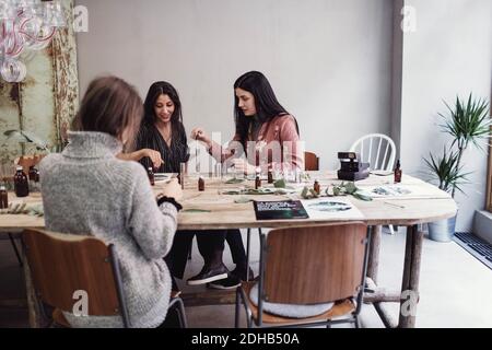 Des collègues femmes préparent le parfum tout en étant assis à table dans l'atelier Banque D'Images