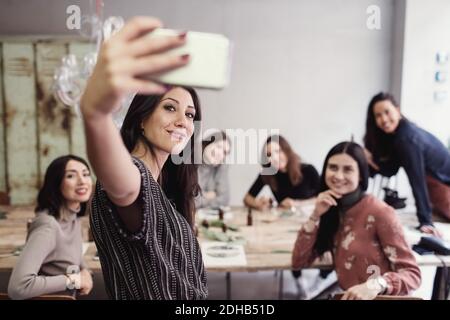Jeune femme souriante prenant le selfie avec des collègues de travail féminins à l'atelier Banque D'Images