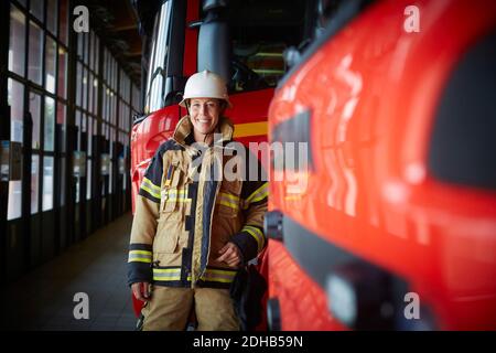 Portrait d'une pompier féminine souriante debout près d'un camion de pompiers à caserne de pompiers Banque D'Images