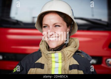 Femme souriante pompier portant un casque qui regarde loin dans la caserne de pompiers Banque D'Images