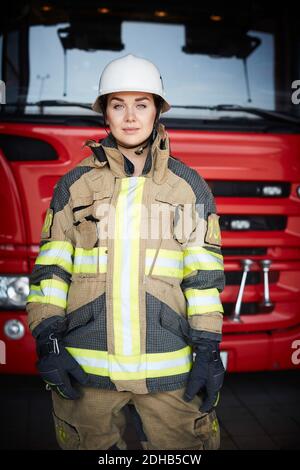 Portrait d'un pompier confiant debout devant un moteur d'incendie à la caserne de pompiers Banque D'Images