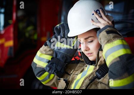 Pompier féminin portant un casque tout en regardant la caserne de pompiers Banque D'Images