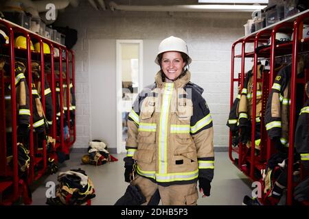 Portrait d'une pompier féminine souriante debout dans le vestiaire à caserne de pompiers Banque D'Images