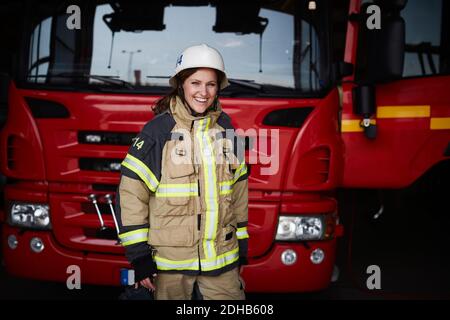 Portrait d'une pompier féminine souriante debout devant le feu moteur à la caserne d'incendie Banque D'Images