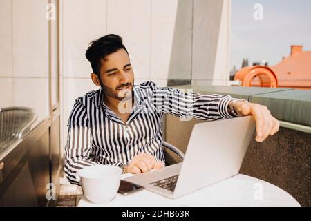 Jeune homme utilisant un ordinateur portable tout en étant assis sur le balcon de l'hôtel Banque D'Images