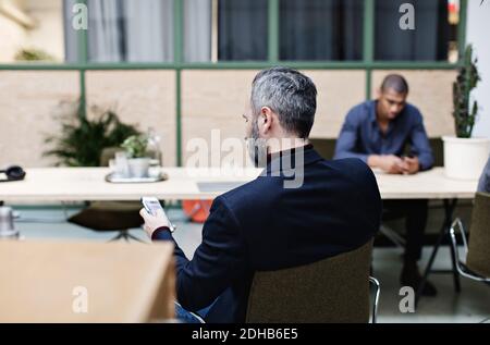 Homme d'affaires mature utilisant un téléphone portable lorsqu'il est assis au bureau Banque D'Images