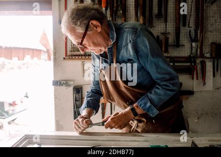 Un homme principal raclage le cadre de la fenêtre sur l'établi au magasin atelier Banque D'Images