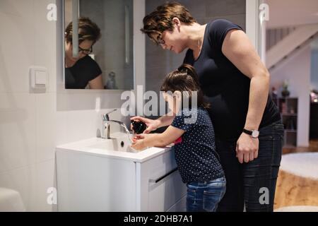 Femme aidant la fille à se laver les mains à l'évier dans la maison Banque D'Images