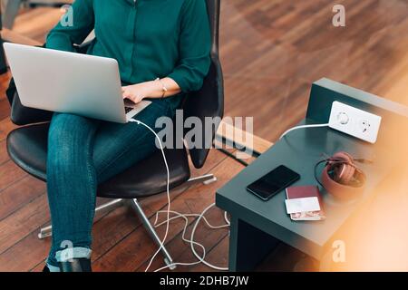 Section intermédiaire d'une femme d'affaires utilisant un ordinateur portable tout en étant assise sur une chaise aéroport Banque D'Images