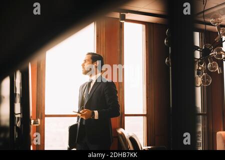 Conseiller financier homme attentif avec casque parlant sur téléphone mobile en vous tenant près de la fenêtre au bureau Banque D'Images