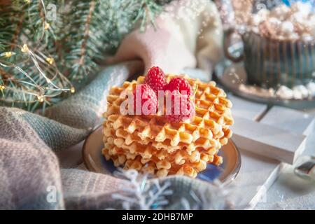 Gaufres viennoises aux framboises et au miel sur la table de Noël avec une tasse de cacao et de guimauve à l'arrière-plan. Banque D'Images