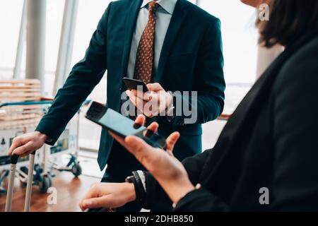 Milieu de section de couple d'affaires utilisant des téléphones mobiles dans l'aéroport Banque D'Images