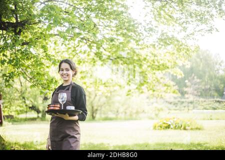 Portrait d'une serveuse jeune femme confiante souriant tout en tenant le service plateau contre les plantes Banque D'Images