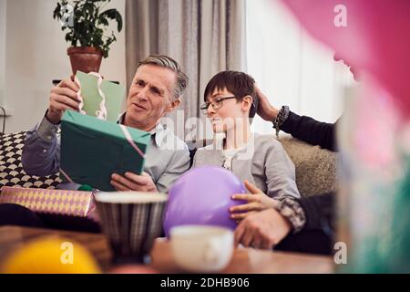 Garçon et grand-père regardant la carte de voeux et le cadeau d'anniversaire tout en étant assis sur un canapé Banque D'Images