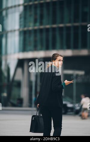 Femme d'affaires regardant sur l'épaule tout en marchant dans la rue en ville Banque D'Images