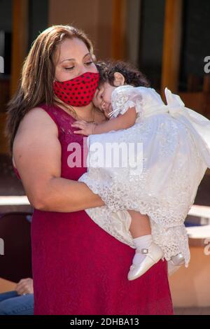 Portant un masque facial en raison de la pandémie du coronavirus, une mère hispanique emmène sa fille à une cérémonie de baptême en plein air dans une Californie du Sud Banque D'Images