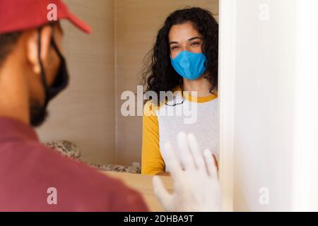 Femme de race mixte portant un masque facial saluant living man à la porte Banque D'Images