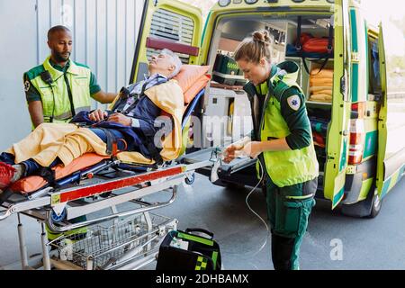 Paramédic avec le patient regardant un collègue préparant l'équipement d'oxygène à l'extérieur ambulance Banque D'Images