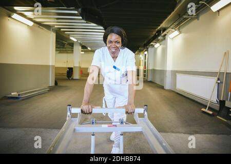 Femme souriante médecin avec un brancard d'hôpital dans un couloir éclairé Banque D'Images