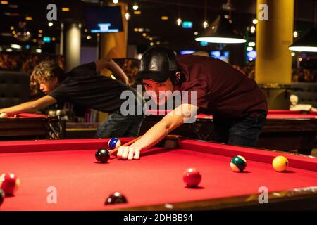 Des adolescents confiants jouant au billard sur des tables rouges éclairées Banque D'Images