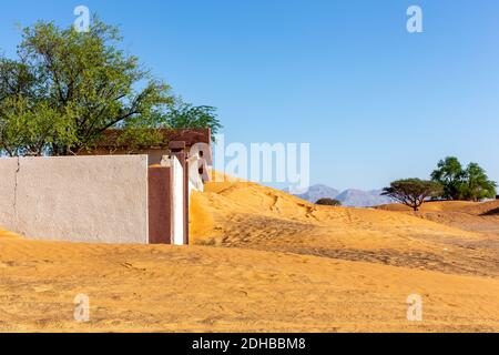 Bâtiment abandonné et clôture enterrée dans le sable dans le village fantôme d'Al-Madame à Sharjah, Émirats arabes Unis, avec des arbres Ghaf sauvages autour. Banque D'Images