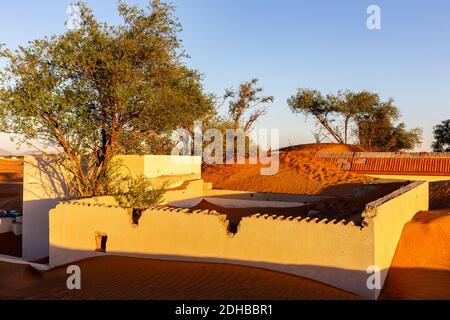 Les bâtiments et les murs de la ville fantôme d'Al Madame enterrés dans des dunes de sable dans le désert de Sharjah, Émirats arabes Unis, coucher de soleil. Banque D'Images