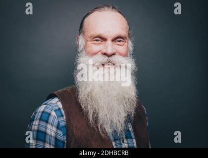 Portrait d'un homme âgé souriant avec une barbe et une moustache blanches sur fond gris Banque D'Images