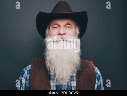 Portrait d'un homme senior à barbe heureux portant un chapeau de cow-boy arrière-plan gris Banque D'Images