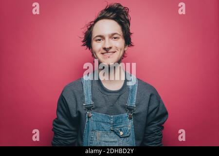 Portrait d'un jeune homme souriant portant une combinaison en denim sur du rose arrière-plan Banque D'Images