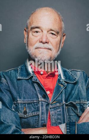 Portrait d'un homme âgé confiant avec les bras croisés contre le gris arrière-plan Banque D'Images