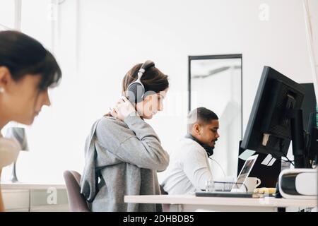 Une femme qui se concentre avec un casque et un ordinateur portable sur le bureau assis avec des collègues au bureau Banque D'Images