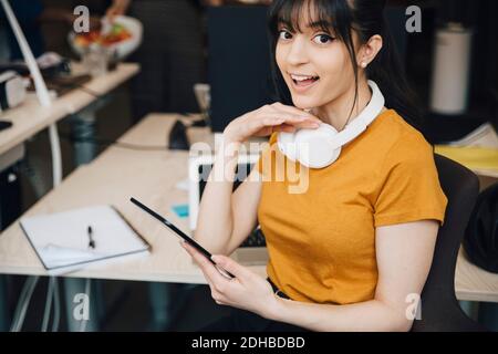 Portrait d'une femme heureuse hacker d'ordinateur à l'aide de la tablette numérique pendant assis au bureau Banque D'Images
