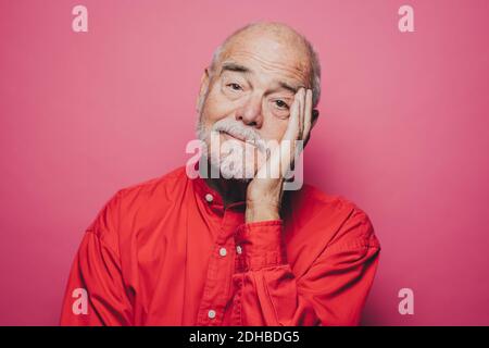 Portrait d'un homme âgé ennuyé avec la tête à la main contre fond rose Banque D'Images