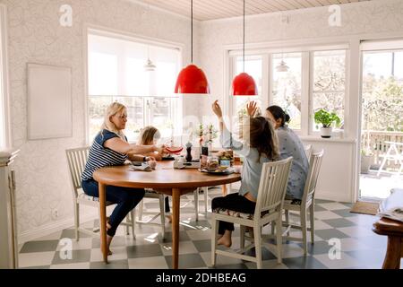 Les mères prenant le petit déjeuner avec leurs filles tout en étant assis à la table à manger en interne Banque D'Images
