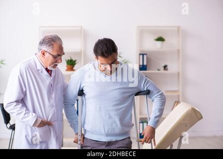 Jeune jambe blessée homme en visite avec un vieux médecin ostéopathe Banque D'Images
