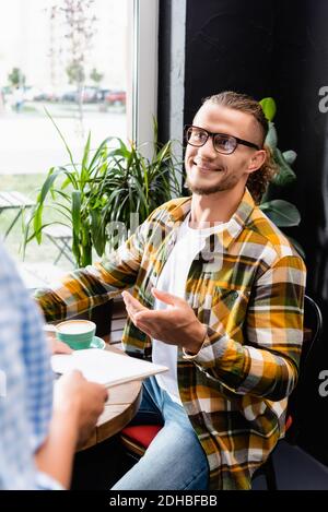 jeune homme souriant dans des lunettes pointant avec le doigt près du serveur sur un premier plan flou Banque D'Images