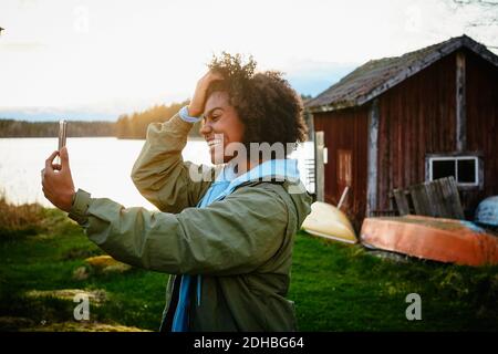 Une jeune femme heureuse qui prend son selfie avec un smartphone debout contre le lac au coucher du soleil Banque D'Images