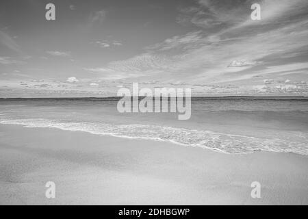 Plage de sable et de vagues en noir et blanc. Vue calme au coucher du soleil en bord de mer. Des vagues calmes éclaboussant l'horizon marin et une ambiance spectaculaire Banque D'Images