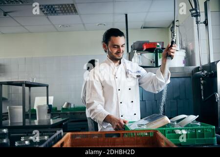 Un jeune chef vaporise de l'eau sur des assiettes dans une cuisine commerciale Banque D'Images