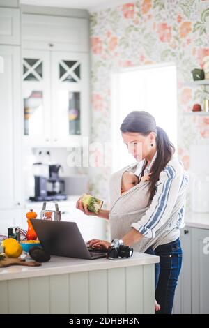 Mère travaillant avec la fille se préparant pour la nourriture blog tout en utilisant ordinateur portable sur cuisine île à la maison Banque D'Images