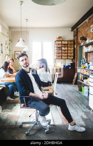 Portrait d'un jeune homme confiant EXPERT EN INFORMATIQUE assis sur une chaise dans le bureau créatif Banque D'Images