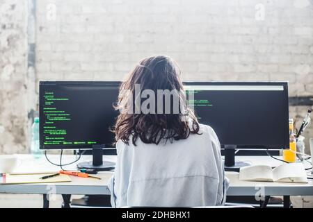 Vue arrière de l'ordinateur de hacker femelle codant au bureau dans bureau créatif Banque D'Images