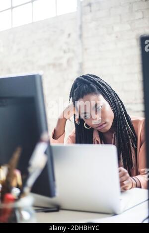 Une femme ingénieuse qui regarde un ordinateur portable au bureau Banque D'Images